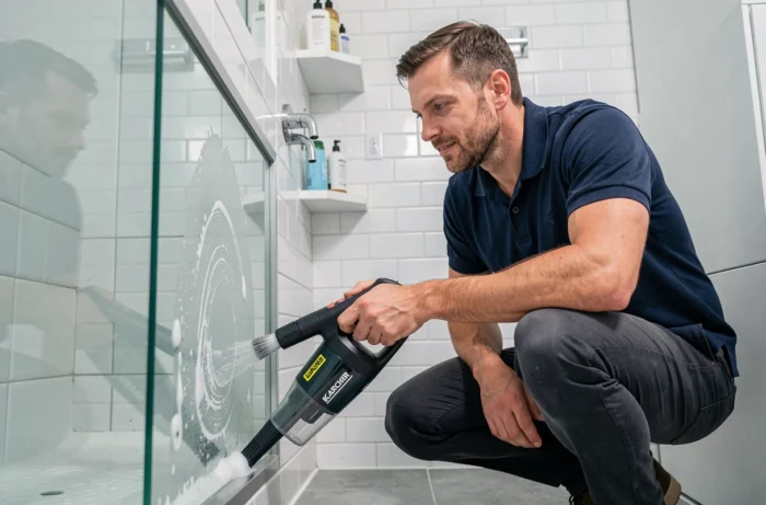 Homme nettoyant un miroir de salle de bain avec un aspirateur de vitres Karcher WV2 dans un intérieur domestique réaliste